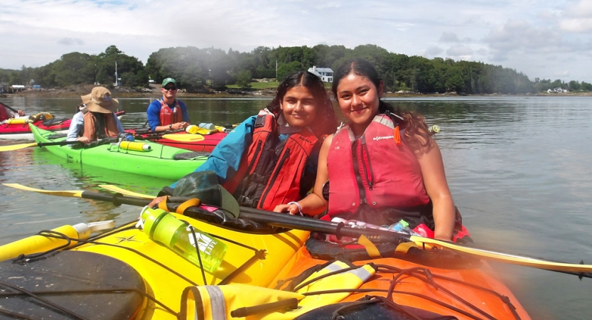 Two people wearing life jackets sit in individual kayaks and smile for the photo